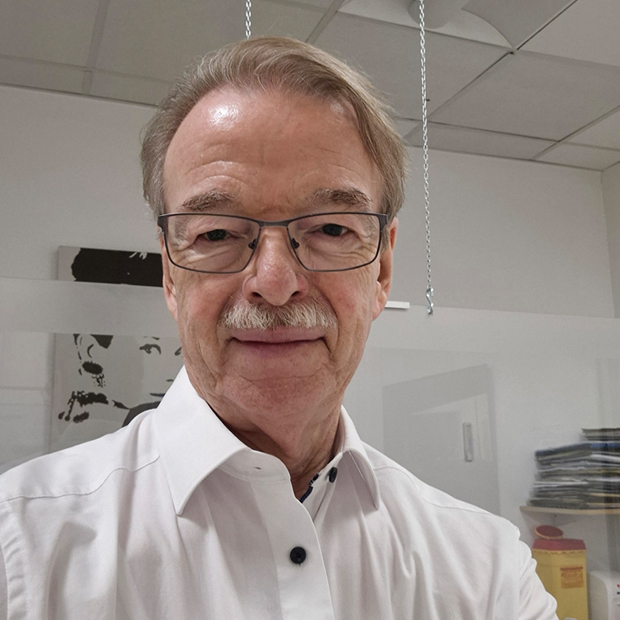 Älterer Herr mit Brille und Schnurrbart blickt freundlich in Kamera.