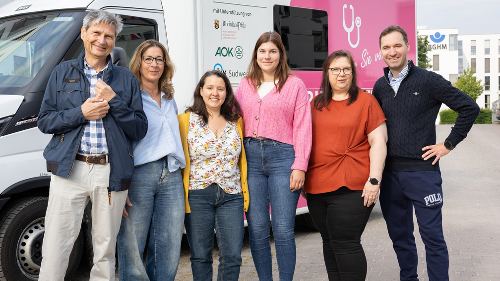 Das Team der Mobilen Arztpraxis 2 Männer und 4 Frauen mittleren Alters, nebeneinander vor einem Transporter, lächeln in die Kamera