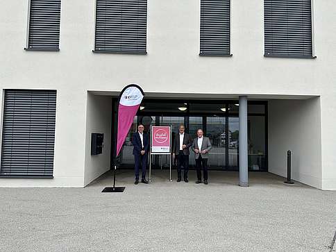 3 Männer in höherem Alter vor stehend vor Neubau in Trier mit Plakataufsteller und Beachflag