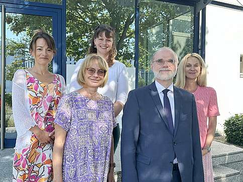 Vier Frauen in Sommerkleidung und ein Mann im Anzug vor einem Gebäude. Sie lächeln in die Kamera.