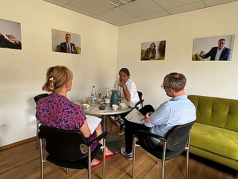 Zwei Männer und eine Frau sitzen an einem runden Tisch und unterhalten sich.